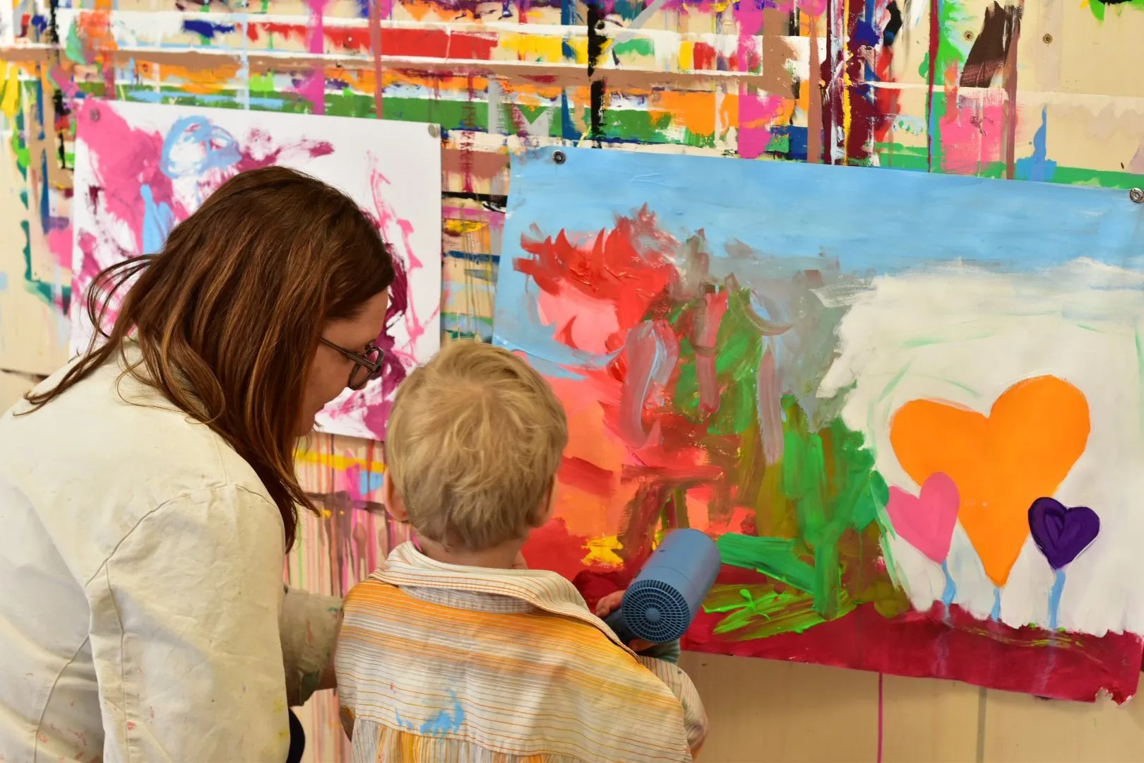 Erwachsene und Kind beim gemeinsamen Malen vor einer farbigen Wand